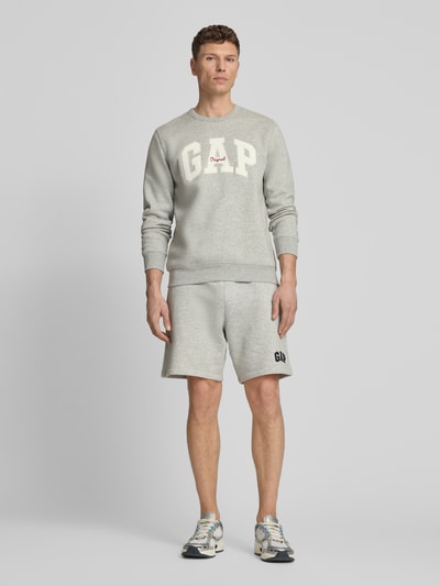 Männermodel trägt Sweatshirt mit Logo und Rundhalsausschnitt van GAP in lichtgrijs katoenmix, regular fit, logoprint, ruglengte 69 cm, mouwlengte 65 cm, ganzkörperansicht van voren.
