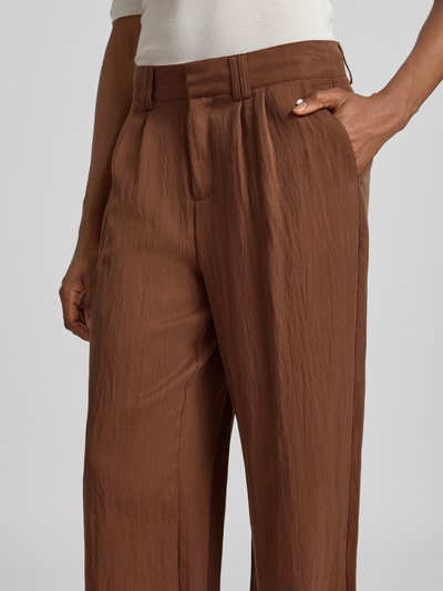Frauenmodel trägt Wide Leg Stoffhose aus Lyocell-Mix Modell 'SOFTTWILL' von Fynch-Hatton in Braun mit Falten und Label-Detail, Nahaufnahme Oberkörper. Damen Stoffhose mit Viskose-Anteil.