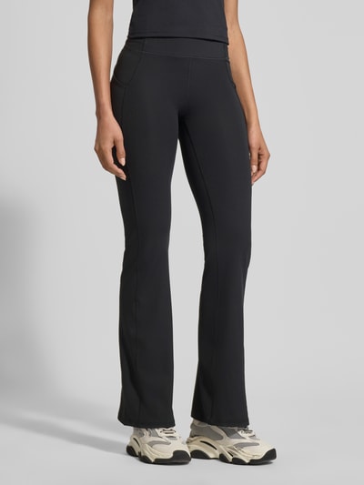 Frauenmodel trägt Flared Fit Leggins mit Logo-Print Modell 'OASIS' von Fabletics in Schwarz, elastischer Bund, glatte Textur, Ganzkörperansicht von vorne.