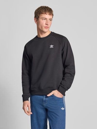 Męski model nosi Regular Fit Sweatshirt aus Baumwoll-Mix od adidas Originals, krój regular fit, kolor jednolity, logo z przodu, okrągły dekolt, krótkie rękawy, wykończenia ściągaczem, materiał bawełniany, widok całej sylwetki z przodu.