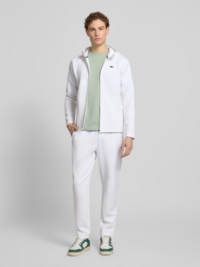 Männermodel trägt Tapered Sweatpants mit Baumwoll-Anteil von Lacoste Sport in Weiß, unifarben, seitliche Reißverschlusstaschen, Ganzkörperansicht von vorne.