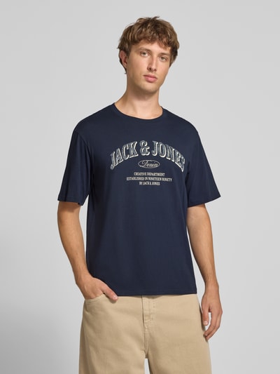 Männermodel trägt Regular Fit T-Shirt aus reiner Baumwolle Modell 'Denver' von JACK & JONES, dunkelblau mit Logo-Print, Nahaufnahme Oberkörper.