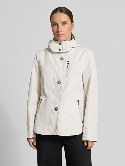 Vrouwenmodel draagt Jacke met kapuze und eingrifftaschen van Gil Bret in regular fit met capuchon, knoopsluiting, ritszakken; ruglengte maat 36: 67 cm, schouderbreedte: 40 cm, borstwijdte: 46 cm, mouwlengte: 64 cm; dames jack in lichte kleur, gladdere stof, details in zilver; ganzekörperaanzicht van voren.
