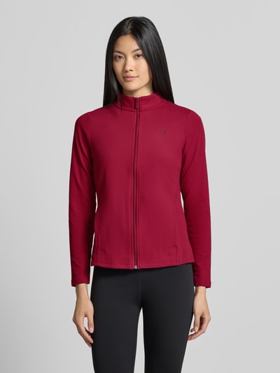 Frauenmodel trägt Slim Fit Trainingsjacke mit Logo-Print von Under Armour in Dunkelrot, schlichter Stil, glatte Textur, Ganzkörperansicht von vorne. Damen Trainingsjacke von Under Armour.