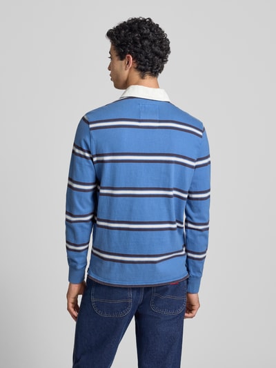 Männermodel trägt Regular Fit Poloshirt mit Logo-Stitching von Superdry in Blau mit weißen und dunklen Streifen, Ganzkörperansicht Rückansicht.