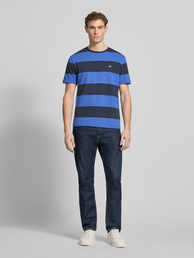 Männermodel trägt Regular Fit T-Shirt mit Logo-Print Modell 'BAR' von Gant, gestreift in Blau, reine Baumwolle, Ganzkörperansicht von vorne.
