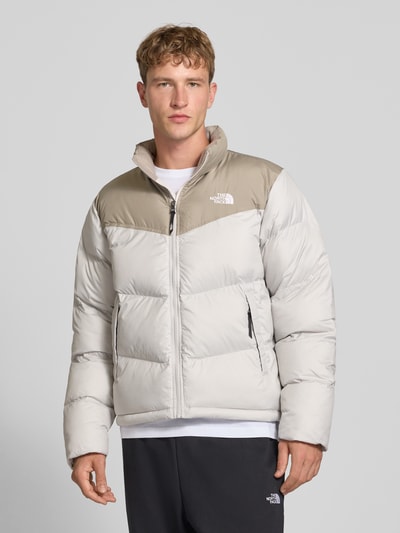 Männermodel trägt Regular Fit Jacke in Stepp-Optik Modell 'SAIKURU' von The North Face in Weiß und Beige, Nahaufnahme Oberkörper. Kontext: Damen Jacke, Logo-Stitching, Stehkragen, Rückenlänge 65 cm, Schulterbreite 47 cm, Brustweite 56 cm, Ärmellänge 67 cm.