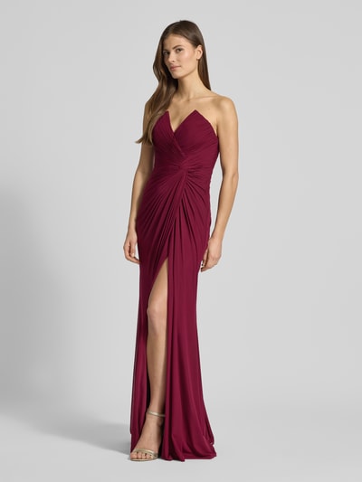 Frauenmodel trägt Regular Fit Abendkleid mit Gehschlitz von Mascara in Bordeaux, Mesh, Raffungen, schulterfrei, blickdichtes Unterkleid, Ganzkörperansicht von vorne.