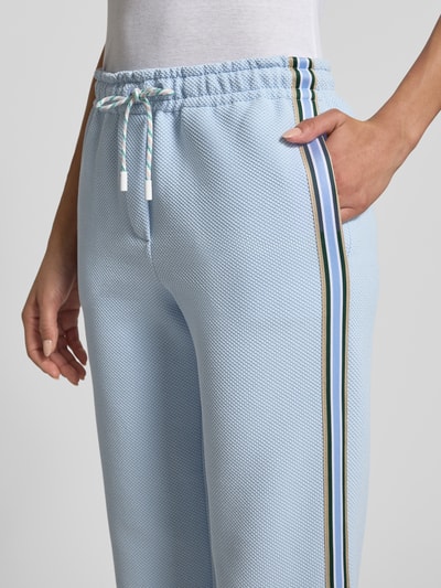 Kobiece model prezentuje spodnie dresowe Wide Fit Sweatpants mit Strukturmuster von Marc Cain, jasnoniebieskie z fakturowanym wzorem i elastycznym pasem z tunelem, boczne lampasy, mieszanka bawełny, szerokość w rozmiarze 36: 39 cm, długość wewnętrzna nogawki 89 cm, zbliżenie na biodra i pas.