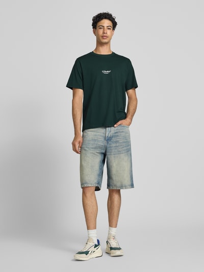 Männermodel trägt dunkelgrünes Herren T-Shirt von Jack & Jones, Reine Baumwolle, Regular-Fit, Logo-Print, Modell 'Soho', Ganzkörperansicht von vorne. Rückenlänge bei Größe M: 61 cm.