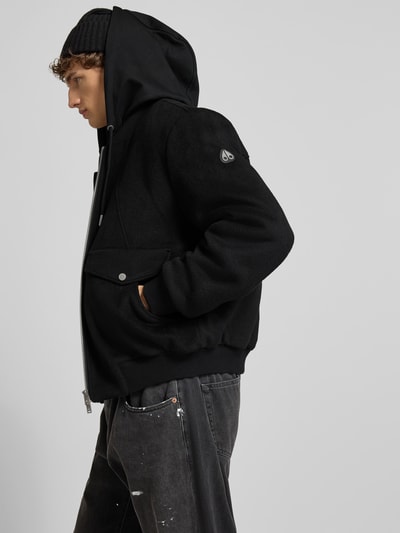 Männermodel trägt schwarze Jacke mit Kapuze von Moose Knuckles aus Woll-Mix, Regular Fit, Reißverschluss, Pattentaschen, Nahaufnahme Oberkörper.