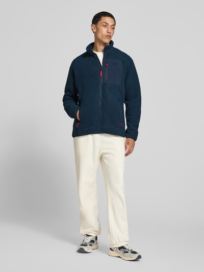 Männermodel trägt Fleecejacke mit Stehkragen von Helly Hansen in Dunkelblau, lockere Passform, Ganzkörperansicht von vorne.