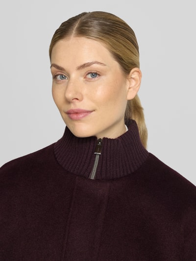 Frauenmodel trägt Mantel aus Woll-Mix mit gestricktem Stehkragen von COMMA in dunklem Lila, sichtbare Struktur, Nahaufnahme Oberkörper. Kontext: Damen Mantel, Woll-Mix mit Viskose-Anteil, Straight Fit, Reiß- und Druckknopfverschluss, seitliche Eingrifftaschen, gestrickte Ärmelabschlüsse, Rückenlänge 92 cm, Schulterbreite 40 cm, Brustweite 60 cm, Ärmellänge 63 cm.
