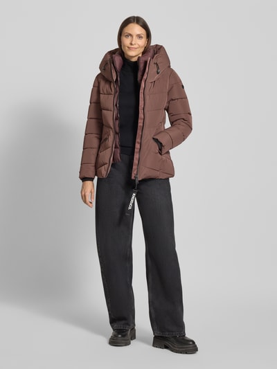 Frauenmodel trägt Steppjacke mit Kapuze von khujo in Braun, Regular Fit, Stehkragen, Reißverschluss, Label-Detail, Reißverschlusstaschen, Rückenlänge 62 cm, Schulterbreite 43 cm, Brustweite 48 cm, Ärmellänge 60 cm, Ganzkörperansicht von vorne.