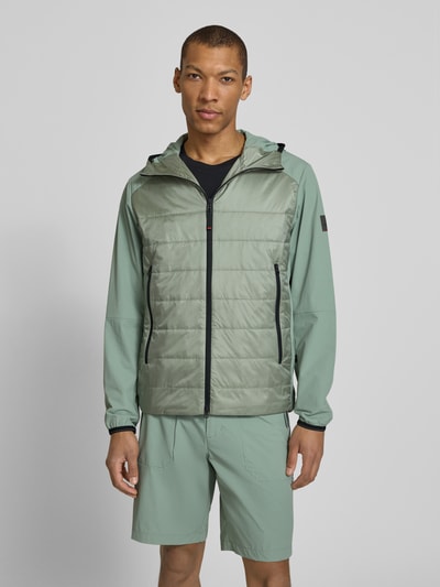 Männermodel trägt Jacke mit Zweiwege-Reißverschluss Modell 'KEGAN2' von FIRE + ICE in hellem Grün, Steppnähte, Kapuze, Ganzkörperansicht von vorne.