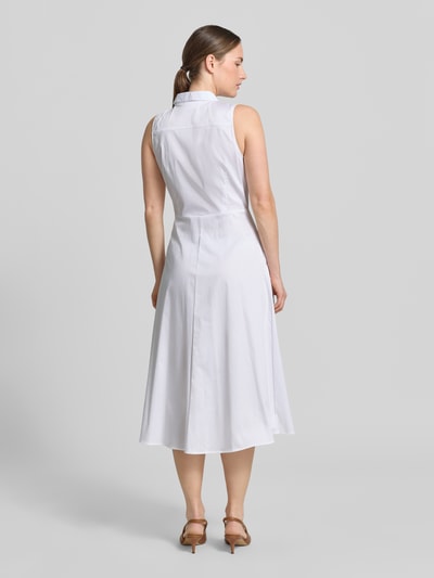 Frauenmodel trägt Hemdblusenkleid aus Satin in Midilänge von Comma im Farbton Weiß mit taillierter Passform aus Baumwoll-Mix, ärmellos, Hemdblusenkragen, durchgängige Knopfleiste und abnehmbarem Taillenband, Rückenlänge bei Größe 36: 120 cm, Brustweite 34 cm, glatte Textur, Ganzkörperansicht Rückansicht.