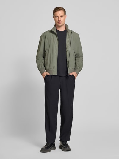 Mannenmodel draagt Relaxed Fit blouson uit waterafstotend materiaal model 'OPENS' van BOSS Orange, look: effen, met opstaande kraag, tweewegritssluiting, labelpatch, lange mouwen met geribde mouwboord, rompzoom geribd, zij-steekzakken, kleur: lichtgroen en zwart, texture: glad textiel, ganzkörperaanzicht van voren.