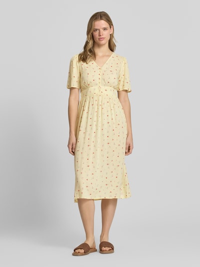 Modelka kobieca ma na sobie A-Linien Midikleid aus reiner Viskose Modell 'TALA' od Pieces, żółty kolor, drobny wzór, gumka, krótki rękaw, dekolt V, długość midi, widok całej sylwetki z przodu.