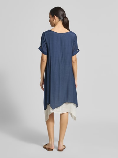 Frauenmodel trägt knielanges Kleid aus Viskose-Mix von Apricot, dunkelblau mit asymmetrischem Saum, lockerer Schnitt, Ganzkörperansicht Rückansicht.