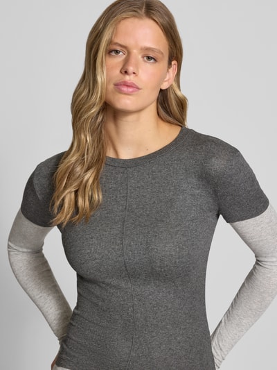 Modelka kobieca ma na sobie Langarmshirt aus Viskose-Mix mit Ripp-Struktur Modell 'Belia' od Topshop, kolor szary, krój slim fit, wzór w prążki, dekolt okrągły, długi rękaw, detaliczny szew, materiał elastyczny, widoczny efekt 2w1, długość tyłu w rozmiarze S: 55 cm, ujęcie: z przodu, zbliżenie na górną część ciała.