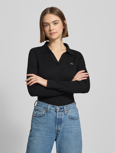 Frauenmodel trägt Longsleeve mit Label-Detail von Calvin Klein Jeans aus schwarzem Baumwoll-Elasthan-Mix, Slim-Fit, Polokragen und V-Ausschnitt, Rückenlänge bei Größe S 57 cm, Nahaufnahme Oberkörper.