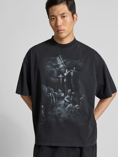 Männermodel trägt Relaxed Fit T-Shirt aus Baumwolle von VETEMENTS in Schwarz mit Destroyed-Look und Motiv-Print, Ganzkörperansicht von vorne.