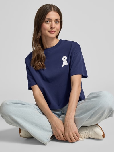 Vrouwenmodel draagt loose fit T-shirt uit puur biologisch katoen model 'ALBERTARAA' van Armedangels, look: effen, regular fit, korte lengte, applicatie: gestikt logo, ronde hals, mouwvorm: korte mouw, materiaalverwerking: jersey, kleur blauw, recht van voren, close-up bovenlichaam.