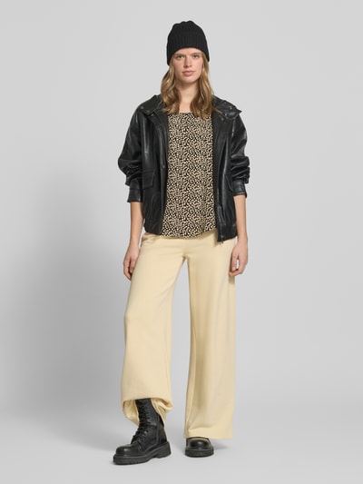 Frauenmodel trägt Regular Fit Blusenshirt aus reiner Viskose Modell 'NOVA' von Only mit Allover-Muster, Rundhals, Kurzarm, helle und dunkle Farbtöne, kombiniert mit heller Hose, Ganzkörperansicht von vorne.