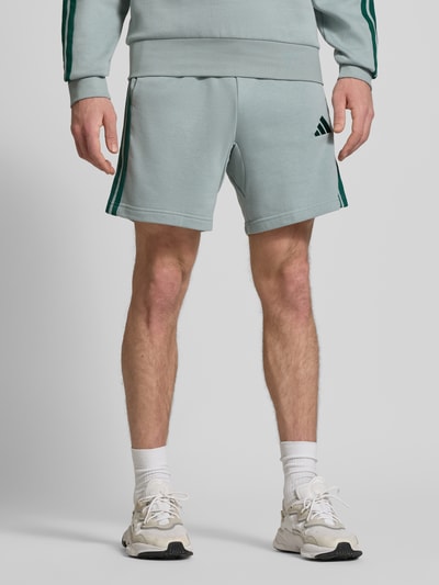 Männermodel trägt Regular Fit Shorts mit Viskose-Anteil von adidas Sportswear, hellgrau mit Logo-Stitching, Baumwoll-Mix, Nahaufnahme Oberkörper.