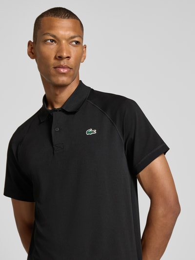 Mężczyznamodel nosi czarne Regular Fit Sport-T-Shirt mit Polokragen od Lacoste, gładka struktura, Herren Sport-T-Shirt von Lacoste Sport, zbliżenie na górną część ciała z przodu.