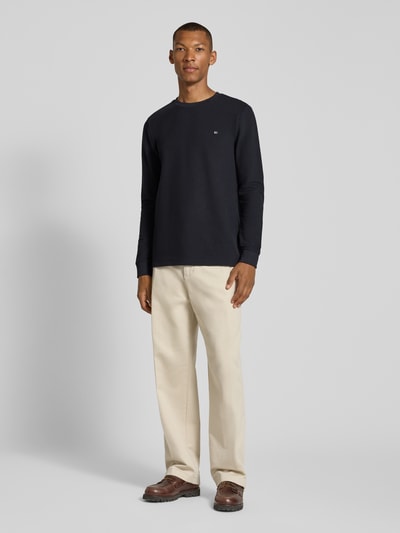 Männermodel trägt Pullover aus Baumwoll-Mix von Christian Berg Men in Schwarz, beiger Hose, glatte Oberfläche, Ganzkörperansicht von vorne, gerader Schnitt, Rundhalsausschnitt, elastische Ärmelbündchen, Rückenlänge bei Größe M 70 cm.