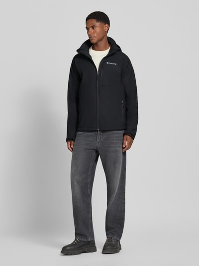Männermodel trägt Regular Fit Jacke mit Logo-Print Modell 'Cascade Ridge™' von Columbia in Schwarz, Softshell-Struktur, Ganzkörperansicht von vorne. Herren Jacke mit Napoleontasche, Kapuze mit Tunnelzug, glatte Textur, Rückenlänge 72 cm, Schulterbreite 44 cm, Brustweite 54 cm, Ärmellänge 82 cm.