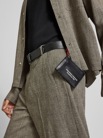 Männermodel trägt Portemonnaie mit Logo-Print von Dsquared2, schwarzes Glattleder mit Logo-Print, Steckfächer, Hauptfach mit Reißverschluss, Ganzkörperansicht von vorne