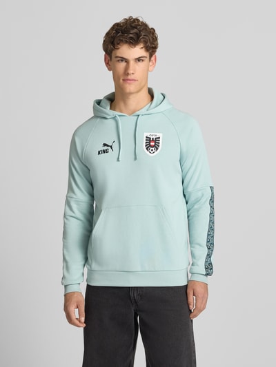 Männermodel trägt Hoodie mit Känguru-Tasche Modell 'ÖFB KING' von PUMA PERFORMANCE in Mint, Baumwoll-Mix, Regular-Fit, Ganzkörperansicht von vorne.