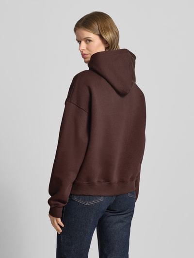 Kobiece model prezentuje Regular Fit Hoodie mit Känguru-Tasche Modell 'Iconic' von Gina Tricot z mieszanki bawełny, krój regular fit, kieszeń kangurka, elastyczne wykończenia, widok całej sylwetki od tyłu.