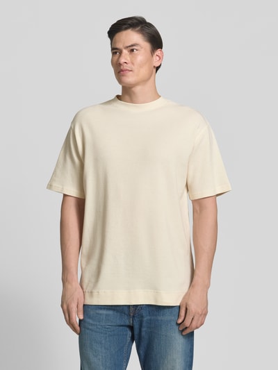 Männermodel trägt Relaxed Fit T-Shirt aus reiner Bio-Baumwolle Modell 'MAARKOS WAFFLE' von Armedangels in Creme, Waffle-Struktur, unifarben, Ganzkörperansicht von vorne.