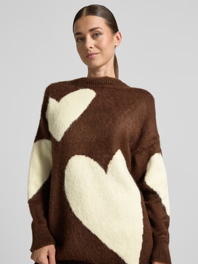 Kobiece model nosi Sweter z dzianiny z mieszanki wełny z alpaki i bawełny miss goodlife, luźny krój, duże kremowe serca, prążkowana stójka, prążkowane wykończenia, długość tyłu w rozmiarze S: 73 cm, długość rękawów: 47 cm, zdjęcie z przodu, zbliżenie na górną część ciała.