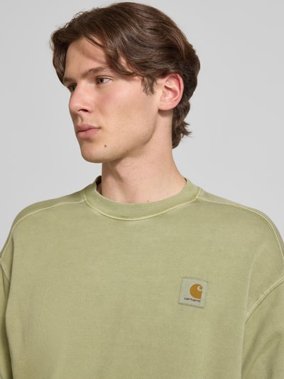 Männermodel trägt Sweatshirt mit Label-Detail Modell 'Nelson' von Carhartt Work In Progress in hellem Grün, Reine Baumwolle, Relaxed-Fit, Rundhalsausschnitt, Nahaufnahme Oberkörper. Rückenlänge bei Größe M: 68 cm, Ärmellänge bei Größe M: 63 cm.
