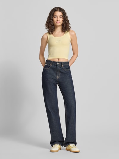 Frauenmodel trägt Slim Fit Top mit Logo-Detail von ANOTHER COTTON LAB in Hellgelb, schlichte Struktur, runder Ausschnitt, Ganzkörperansicht von vorne.