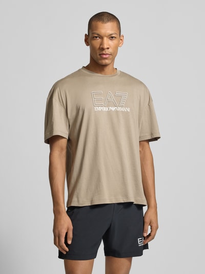 Mannelijk model draagt T-shirt met logo en ronde hals van EA7 Emporio Armani, puur katoen, regular fit, ruglengte maat M 68 cm, frontale borst-nahaufnahme.