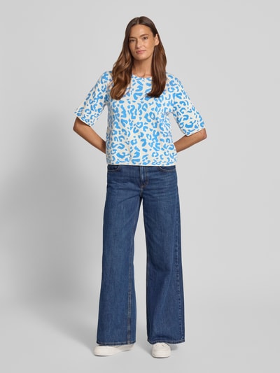 Frauenmodel trägt Relaxed Fit Shirt aus Viskose-Anteil Modell 'Mayas' von Vila mit blau-weißem Allover-Animal-Print, Strick-Optik, Halbarm, Rundhalsausschnitt, Material-Mix, Ganzkörperansicht von vorne.