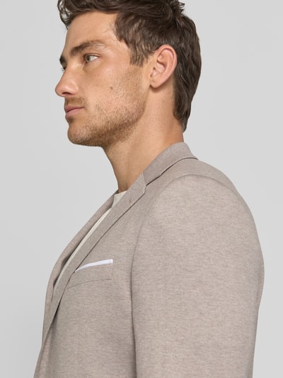 Męski model nosi Regular Fit Blazer aus Viskose-Mix model 'Finch' von JOOP! Collection w jasnobeżowym kolorze, elastyczna mieszanka wiskozy, krój regular fit, brustasza, kołnierz z połami, kieszenie z patką, listwa z 2 guzikami, długość tyłu w rozmiarze 50: 73 cm, szerokość ramion w rozmiarze 50: 38 cm, długość rękawów w rozmiarze 50: 64 cm, zbliżenie na górną część tułowia z przodu.