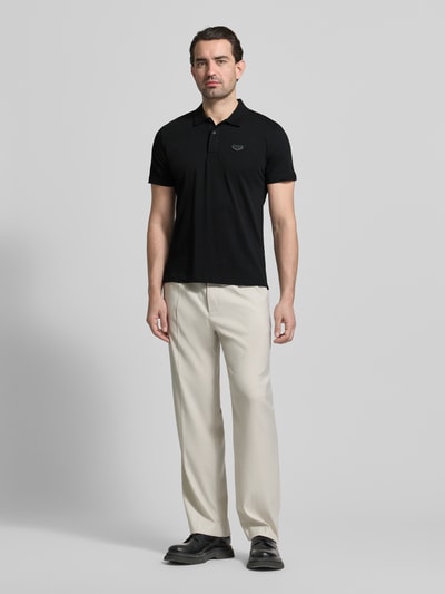 Männermodel trägt Slim Fit Polo-Shirt mit Logo-Applikation von Antony Morato, reine Baumwolle, Polo-Kragen, schwarze Farbe, Ganzkörperansicht von vorne.