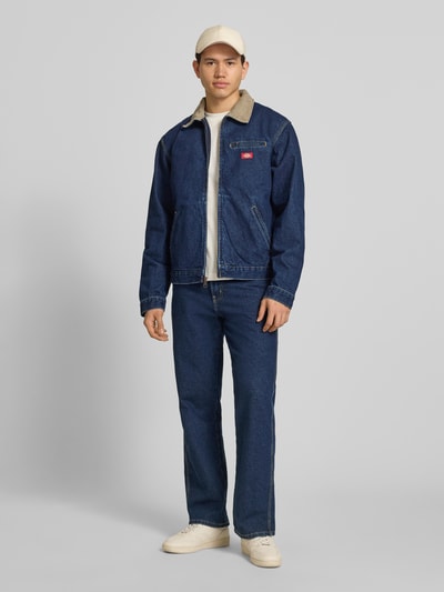 Männermodel trägt Jeansjacke mit Label-Detail und Reißverschluss von Dickies, Reine Baumwolle, Regular-Fit, Umlegekragen, Eingrifftaschen, Ganzkörperansicht von vorne.