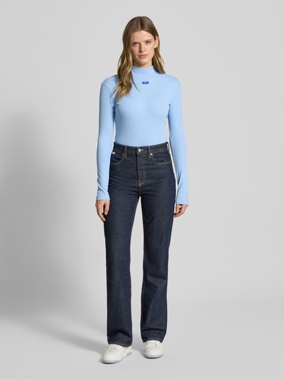 Frauenmodel trägt Slim Fit Langarmshirt aus Baumwoll-Mix Modell 'EASY' von Hugo Blue in Hellblau, hochgeschlossen, Rippstrick, Ganzkörperansicht von vorne.