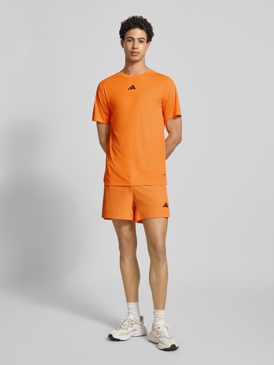 Männermodel trägt Regular Fit Shorts mit Logo-Print Modell 'Power' von adidas Training, Strukturmuster, Elastischer-Material-Mix, Eingrifftaschen, Elastischer Bund, leuchtend orange Farbe, Ganzkörperansicht von vorne.