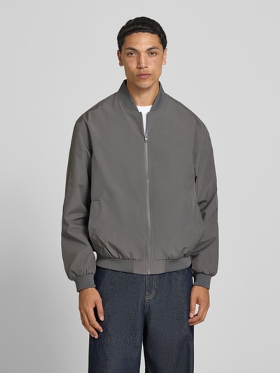Männermodel trägt Herren Bomberjacke mit Stehkragen Modell 'CHARGE' von Jack & Jones, grauer Regular-Fit, Reißverschluss, Ganzkörperansicht von vorne. Rückenlänge bei Größe M: 67 cm, Schulterbreite: 53 cm, Brustweite: 62 cm, Ärmellänge: 65 cm.