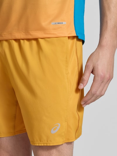 Męski model nosi Regular Fit Shorts z wewnętrznymi figami Model 'Core' od ASICS TIGER, żółty, nadruk z logo, elastyczny pas, Szerokość w rozmiarze M: 38 cm, Długość wewnętrzna nogawki w rozmiarze M: 17 cm, zbliżenie na górną część nóg