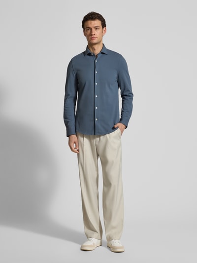 Mężczyzna nosi Shaped Fit Freizeithemd aus reiner Baumwolle von Marc O'Polo w kolorze jednolitym, krój shaped fit, bawełna piké, długi rękaw, cutaway kołnierz, mankiet na jeden guzik, zdjęcie całopostaciowe z przodu.