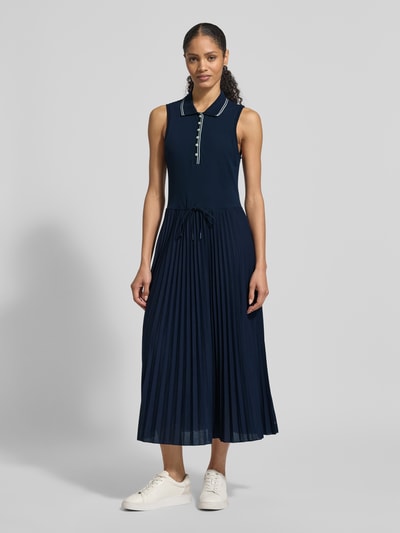 Modelka nosi Tailliertes Freizeitkleid aus Baumwoll-Mix od Tommy Hilfiger, granatowa, plisowana spódnica, długość midi, góra dzianinowa, kołnierzyk polo, guziki z przodu, szerokie ramiączka, widok całej sylwetki z przodu.